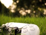 a wii remote laying in the grass with trees in the background