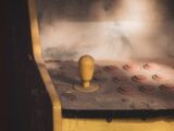 Close-up of a dusty vintage arcade machine control panel with joystick and buttons, evoking nostalgia.