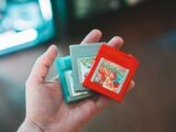 person holding red and green nintendo game cartridge