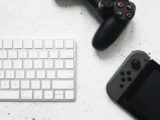 Close-up of a wireless keyboard and gaming controllers on a marble surface.