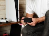 A man sitting on a desk holding a small device