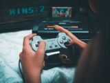 Close-up of hands holding vintage Sony controller with Sega Mega Drive in background.