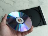 Hand holding a shiny cd with a case behind.