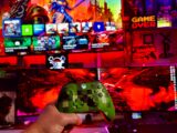 Person holding a video game controller in front of screens.