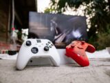 White and red Xbox wireless controllers set outdoors. A computer screen is blurred in the background.