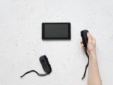 A person holds a Joy-Con controller with a Nintendo Switch on a white textured surface.