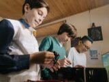 Three teenagers collaborate on a computer project indoors, focusing on microchips and technology.
