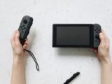 Close-up of hands holding a Nintendo Switch and Joy-Con controllers on a white surface.