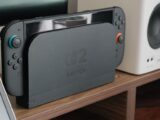 Nintendo console docked among speakers and a monitor on a wooden shelf.