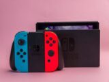 Close-up of Nintendo Switch console with red and blue Joy-Con controllers on pink background.