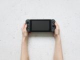 Top view of hands holding a portable gaming console against a textured white background.