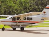 A small aircraft parked on a tarmac surrounded by lush greenery under daylight.