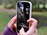 Hands holding a smartphone, taking a picture of a forest.