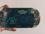 Close-up of a hand holding a PlayStation Vita with Ratchet & Clank displayed on screen. Captured in Johannesburg.