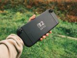 Hand holding a black nintendo switch lite outdoors